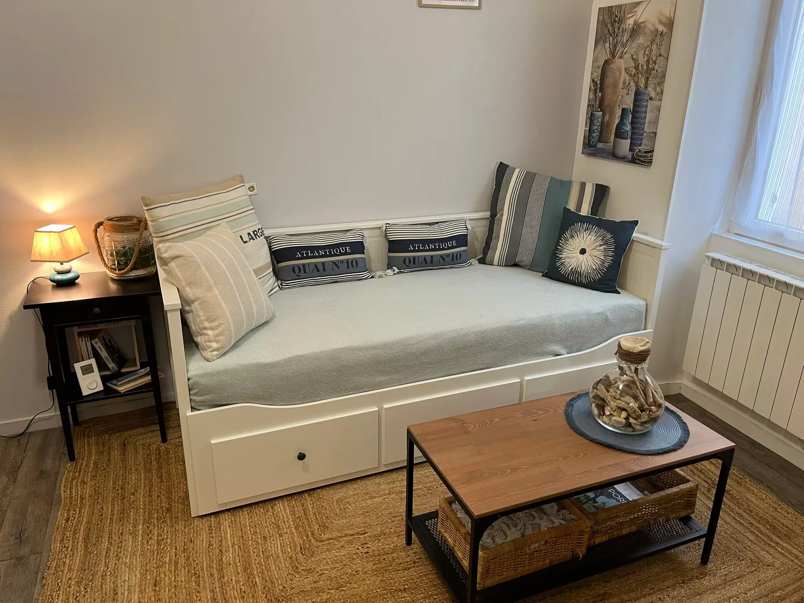 Pièce à vivre du Nid Galipaud : canapé-lit blanc, coussins marins, table basse et tapis en jute