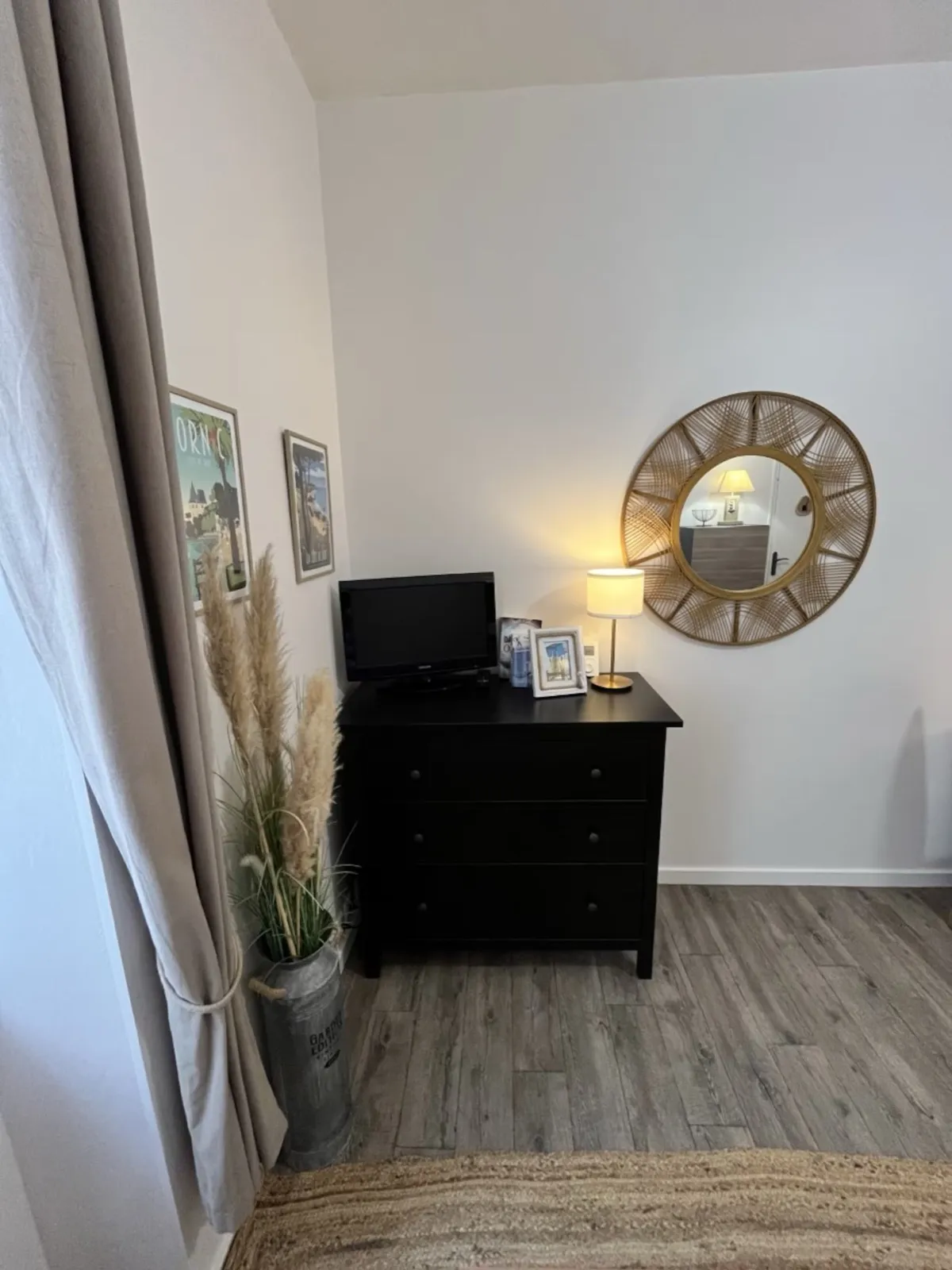 Commode noire avec la télévision, lampe et affiches de Pornic au mur